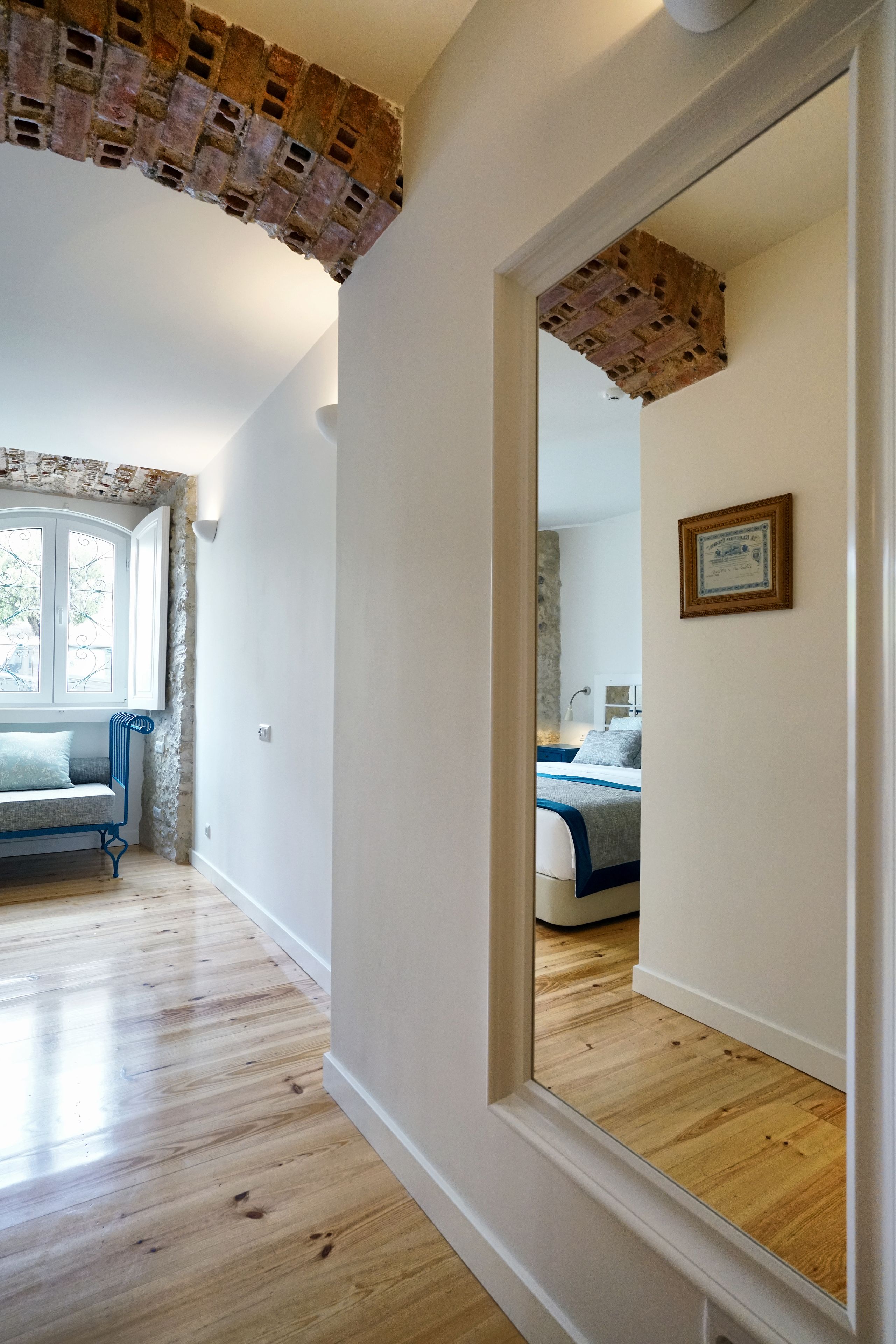 Un pasillo con suelo de madera, un banco azul y una ventana con cortinas blancas.