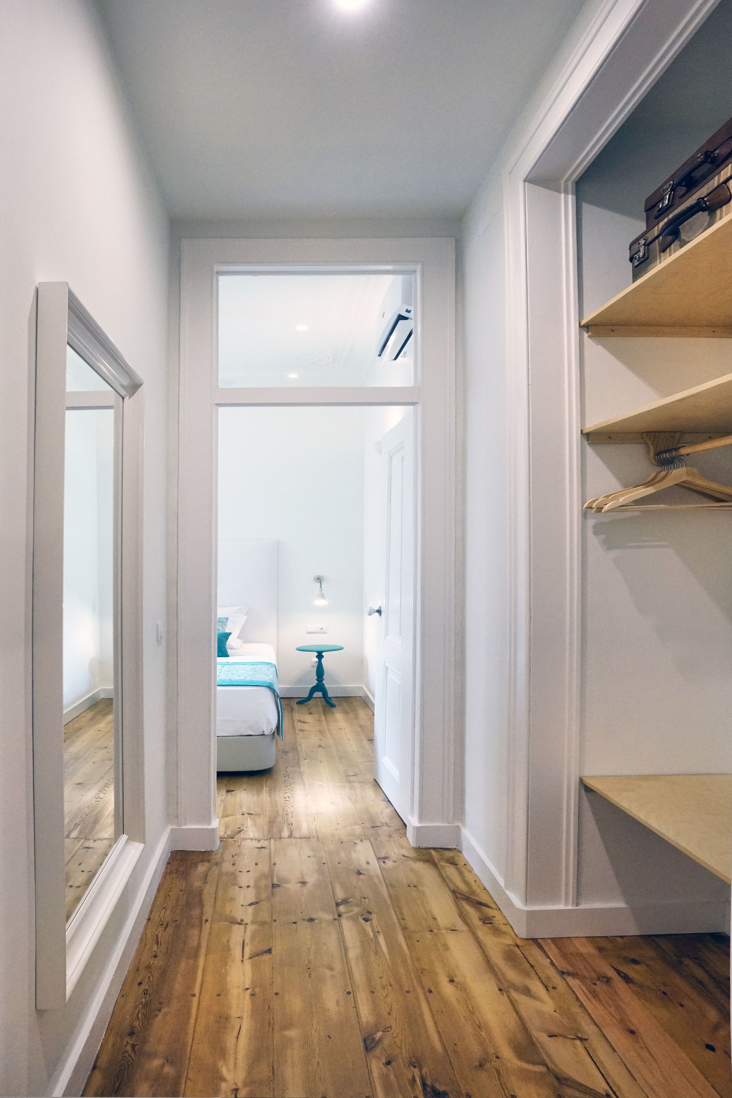 Un pasillo estrecho con suelo de madera, paredes blancas y un armario con estantes.