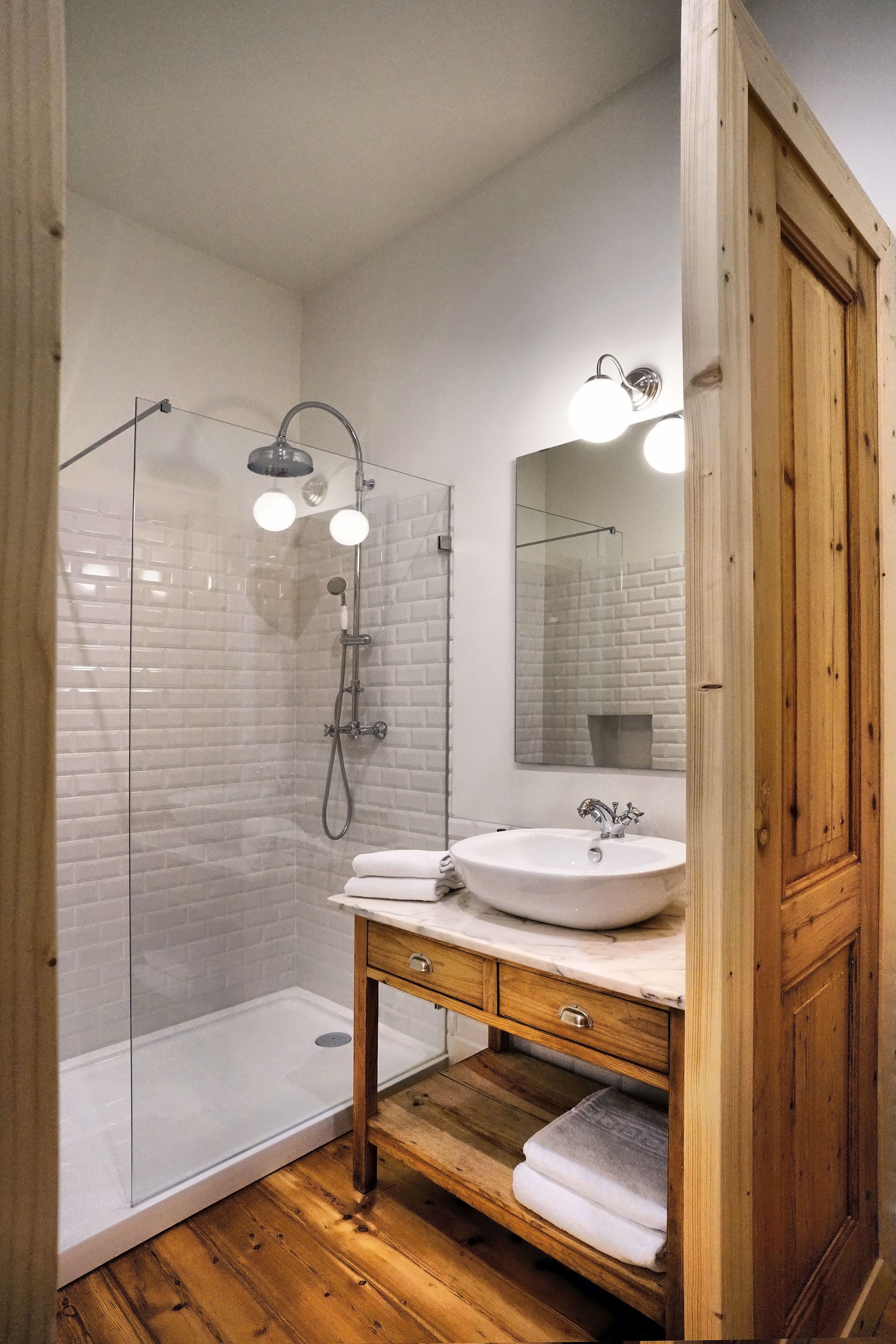 A bathroom with a glass-enclosed shower, a white sink with a marble countertop, and wooden cabinetry.