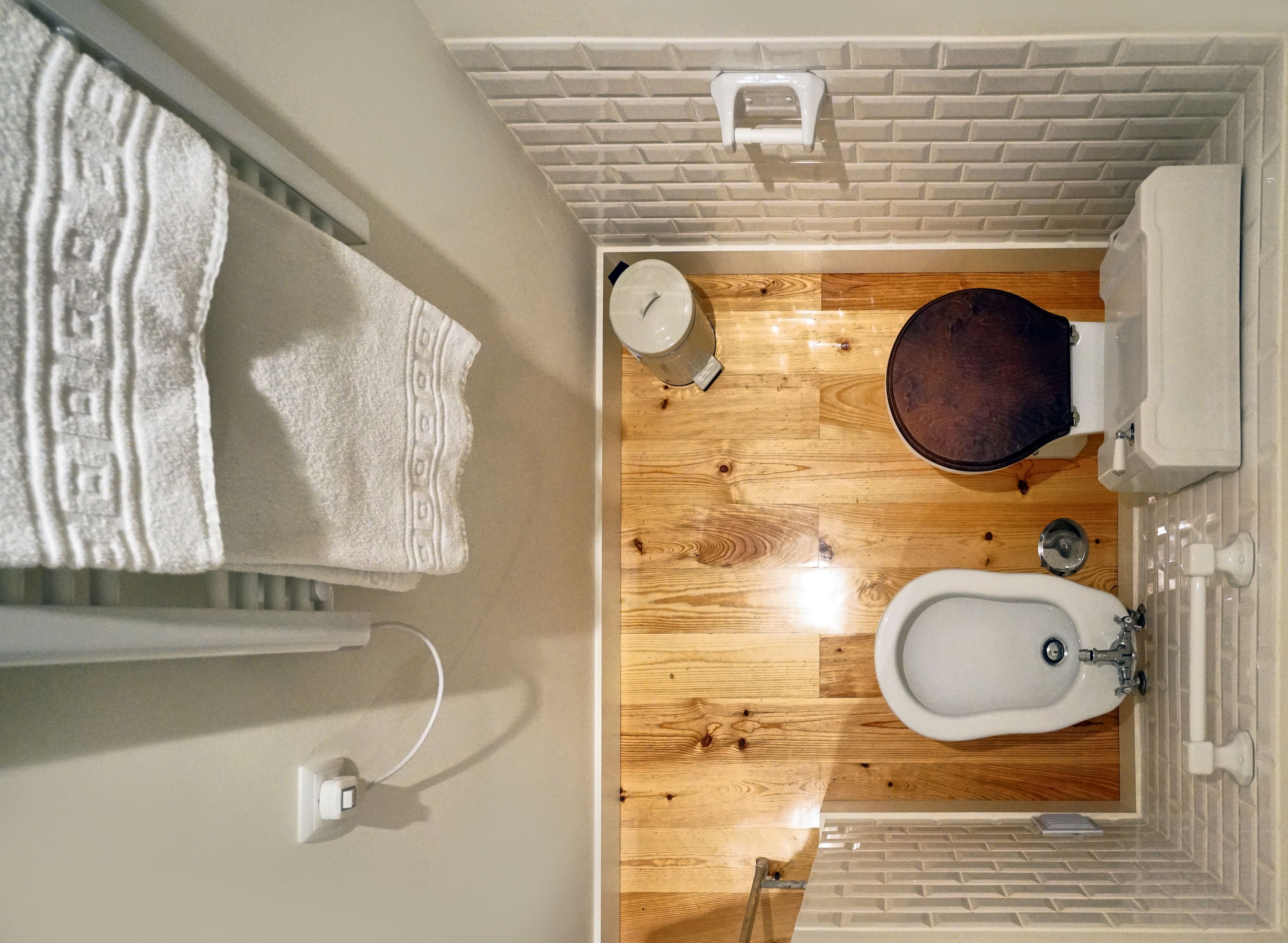 Un bagno con pavimento in legno, sanitari bianchi e un asciugamano appeso al muro.