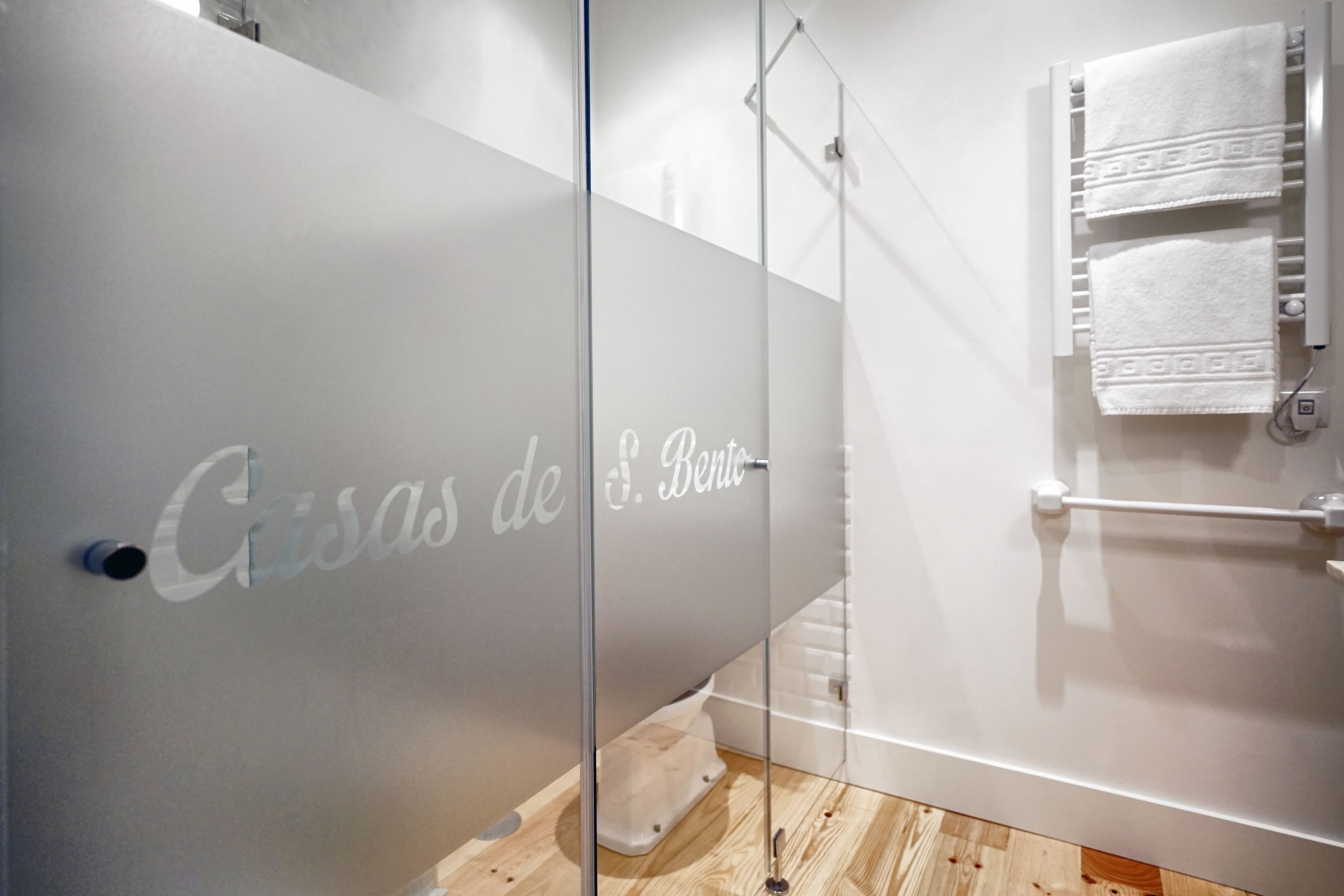A modern bathroom with a glass partition, a towel rack, and a wooden floor.