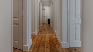 Un largo pasillo estrecho con suelo de madera y paredes blancas, que conduce a una puerta al final.