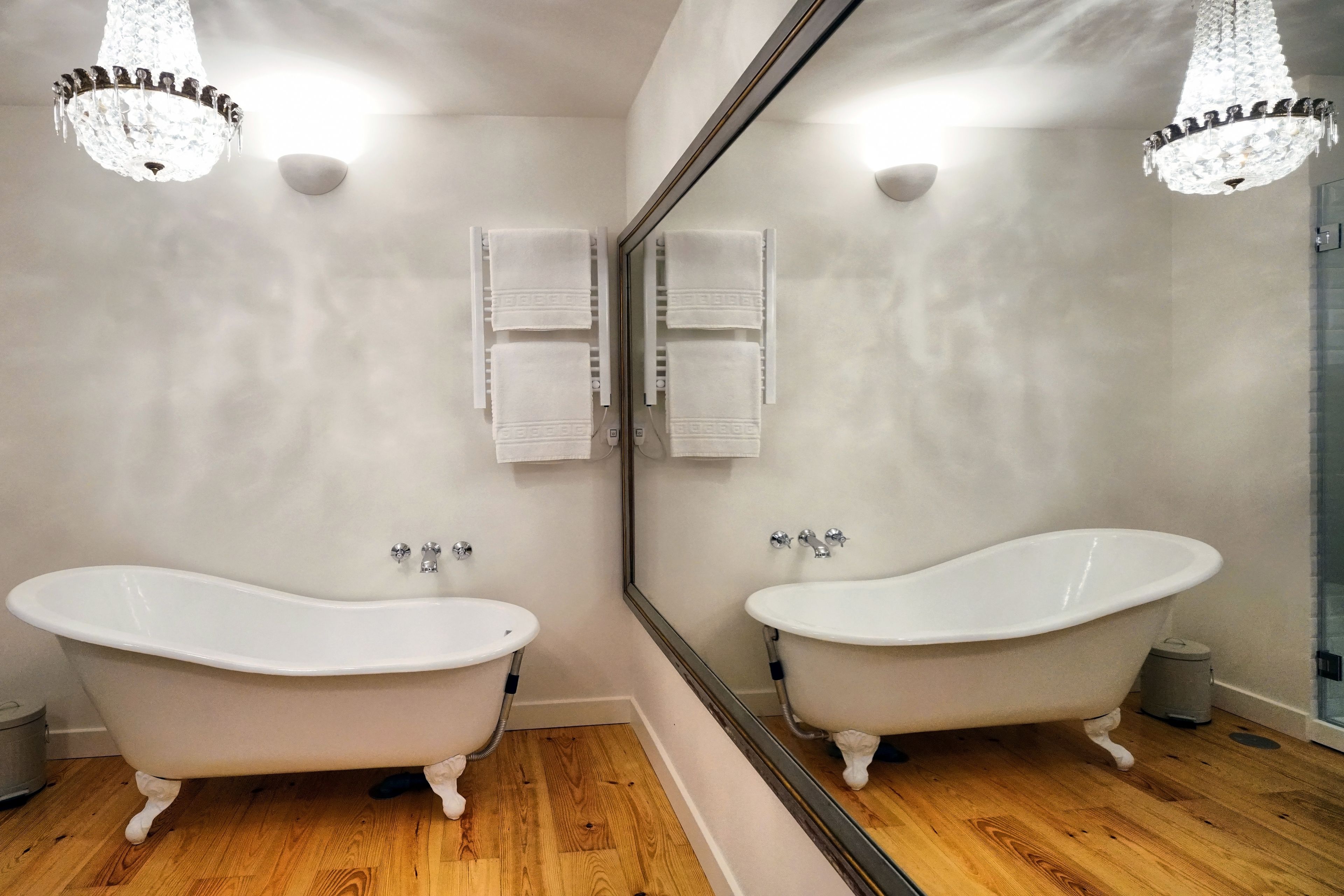 A bathroom with two clawfoot tubs, a large mirror, and a chandelier.