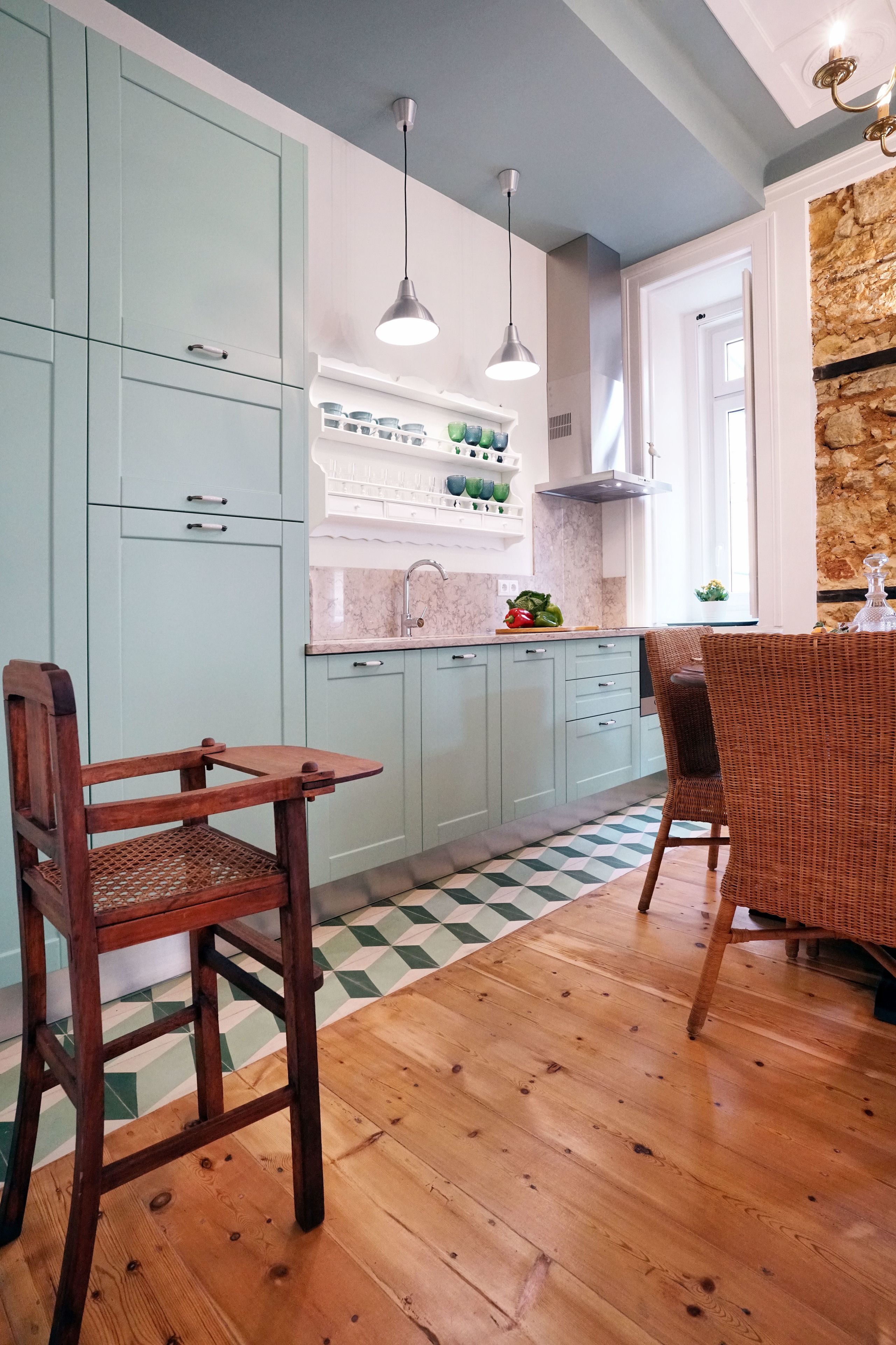 Een keuken met lichtblauwe kastjes, een houten eettafel en twee rieten stoelen.