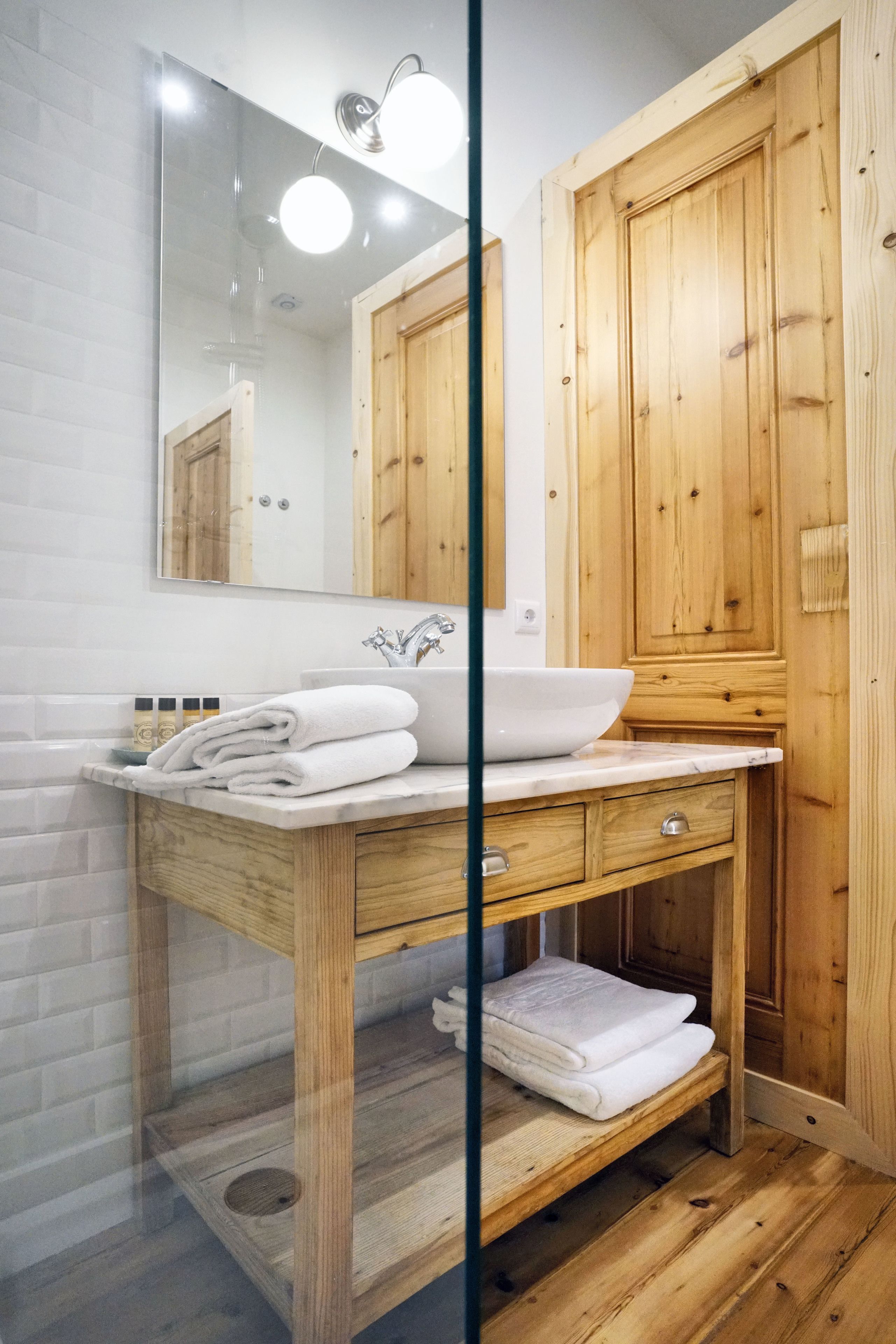 Een badkamer met een houten wastafel, een witte wasbak en een grote spiegel.