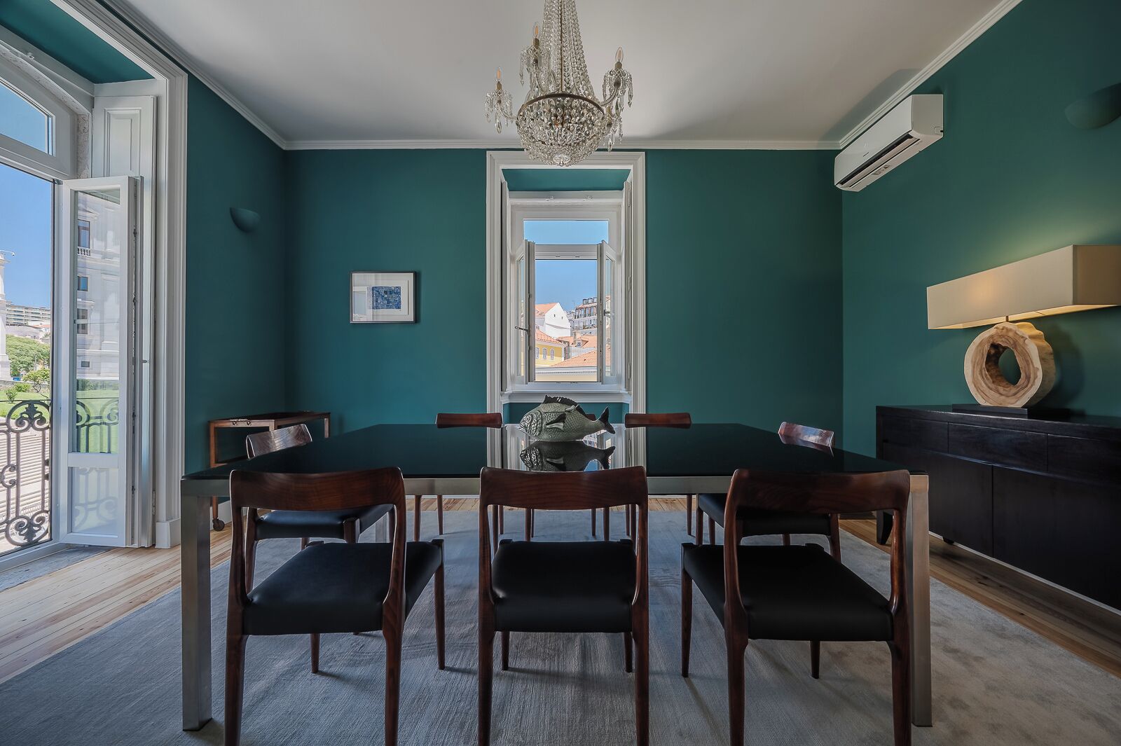 A dining area with a table and chairs, a chandelier, and a view through a window.