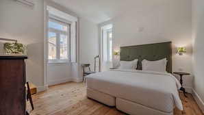 Un dormitorio con una cama grande, suelo de madera y vistas a edificios por la ventana.