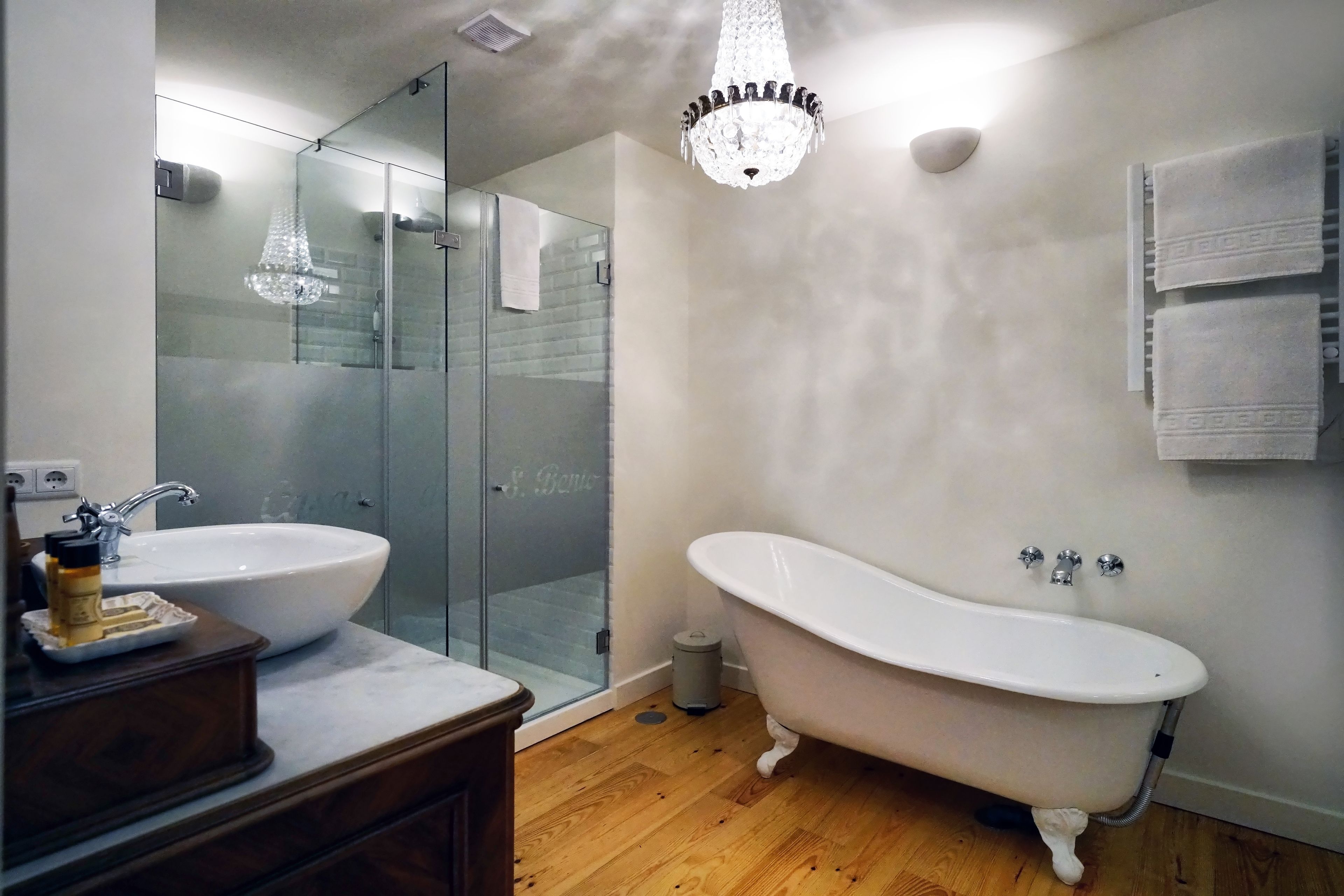 A bathroom with a freestanding bathtub, a glass-enclosed shower, a white sink, and a wooden vanity.