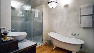 A bathroom with a freestanding bathtub, a glass-enclosed shower, a white sink, and a wooden vanity.