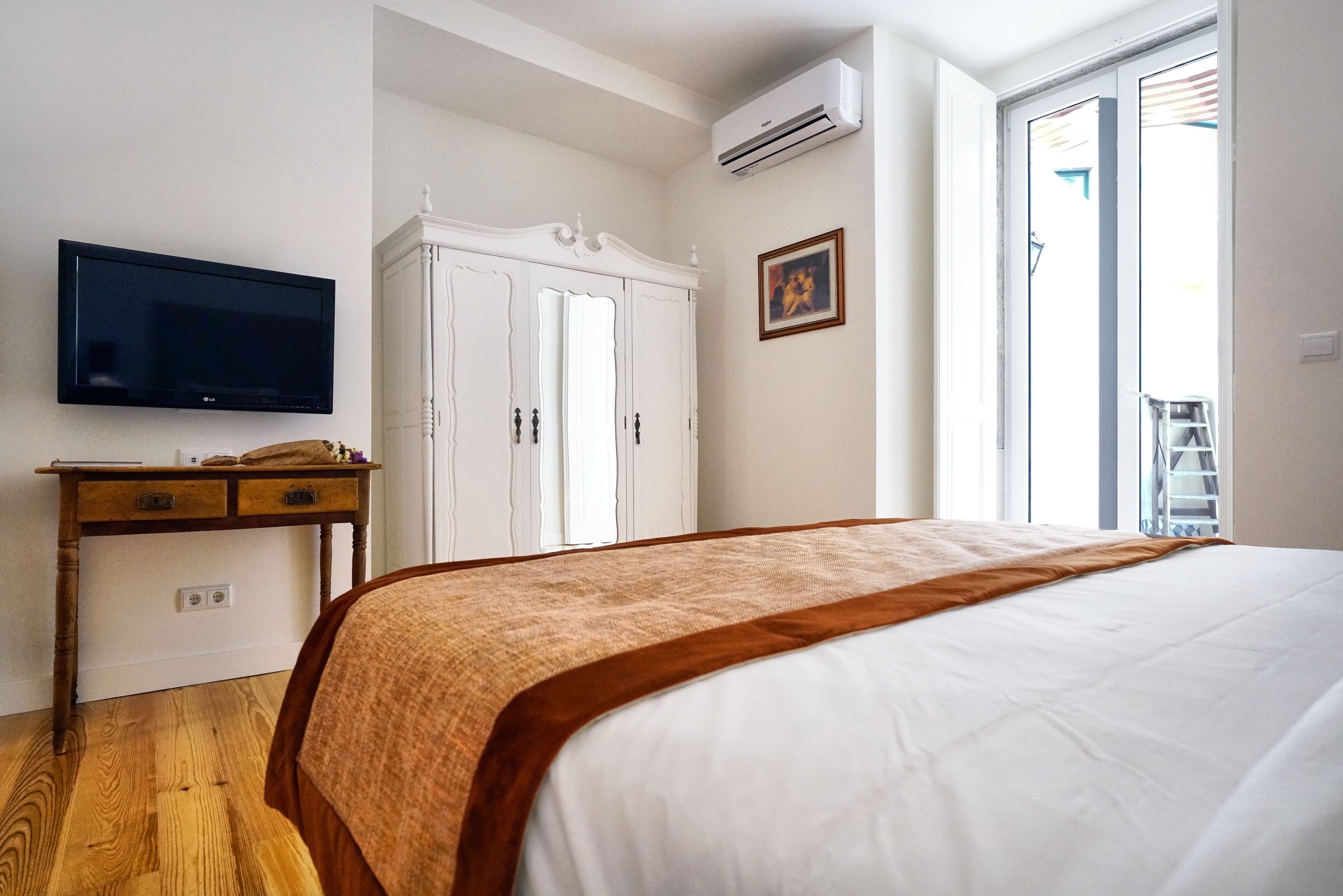 A bedroom with a bed, a TV, a wardrobe, and a window.