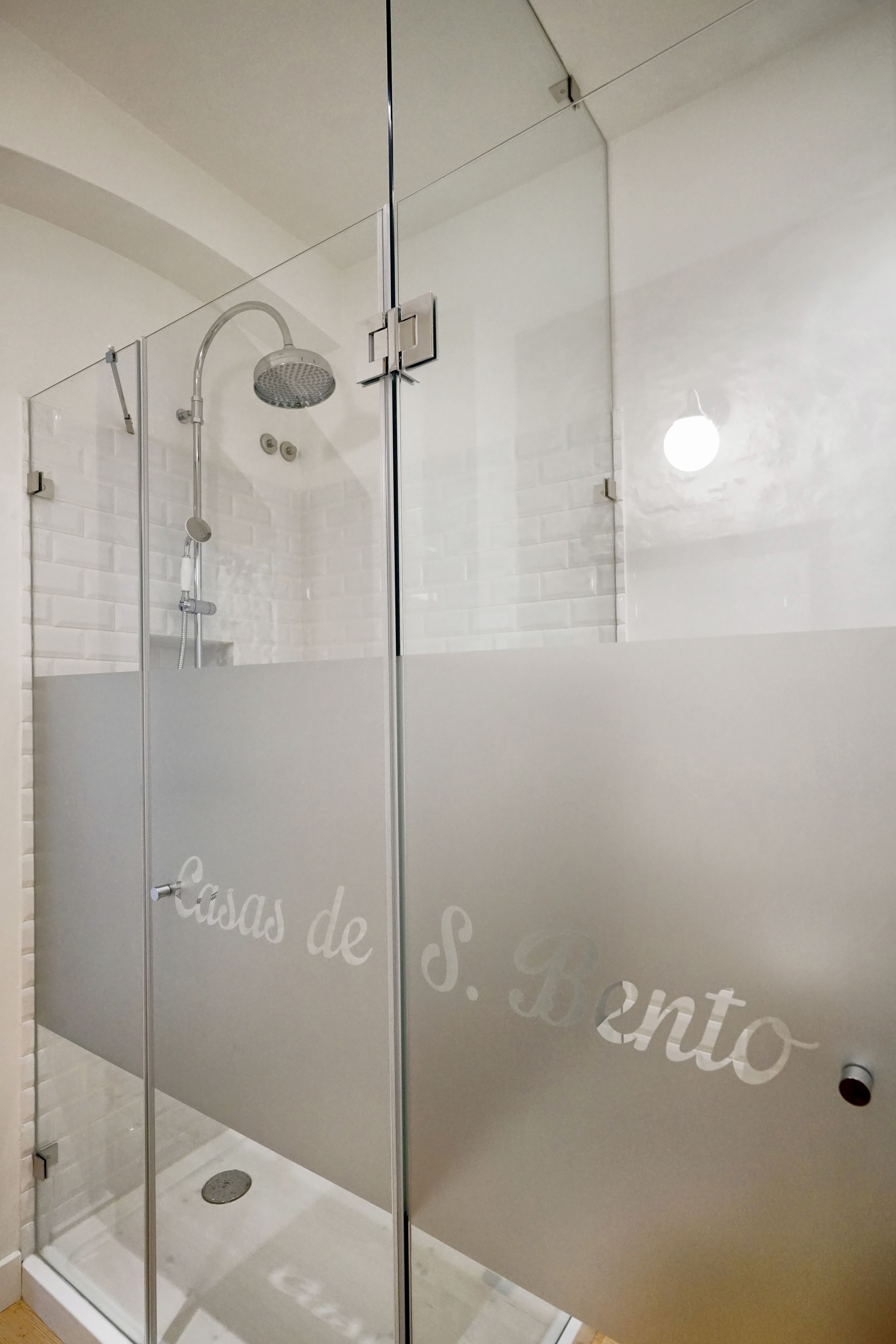 Un espace douche clos par des parois en verre, avec une porte en verre dépoli et une pomme de douche.