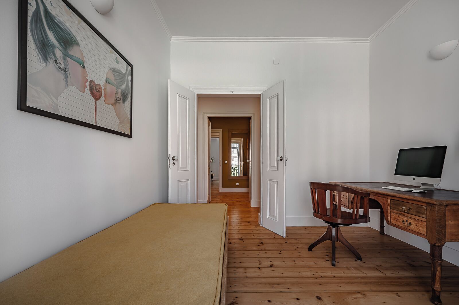Una habitación con una cama, un escritorio con una computadora y una puerta que da a otra estancia.
