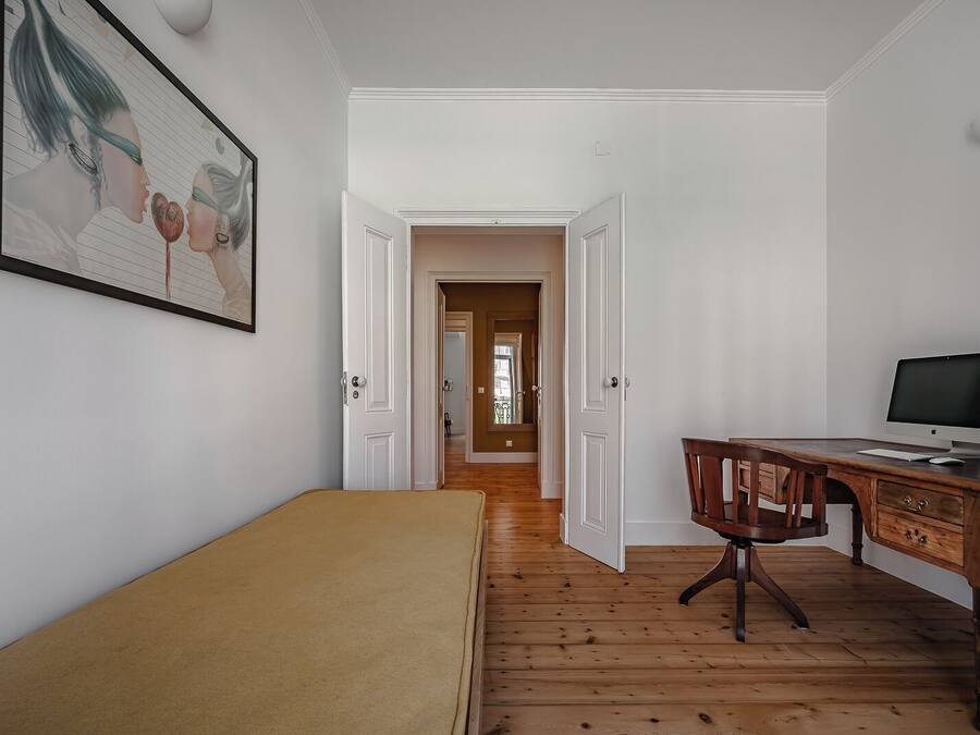 Una habitación con una cama, un escritorio con una computadora y una puerta que da a otra estancia.