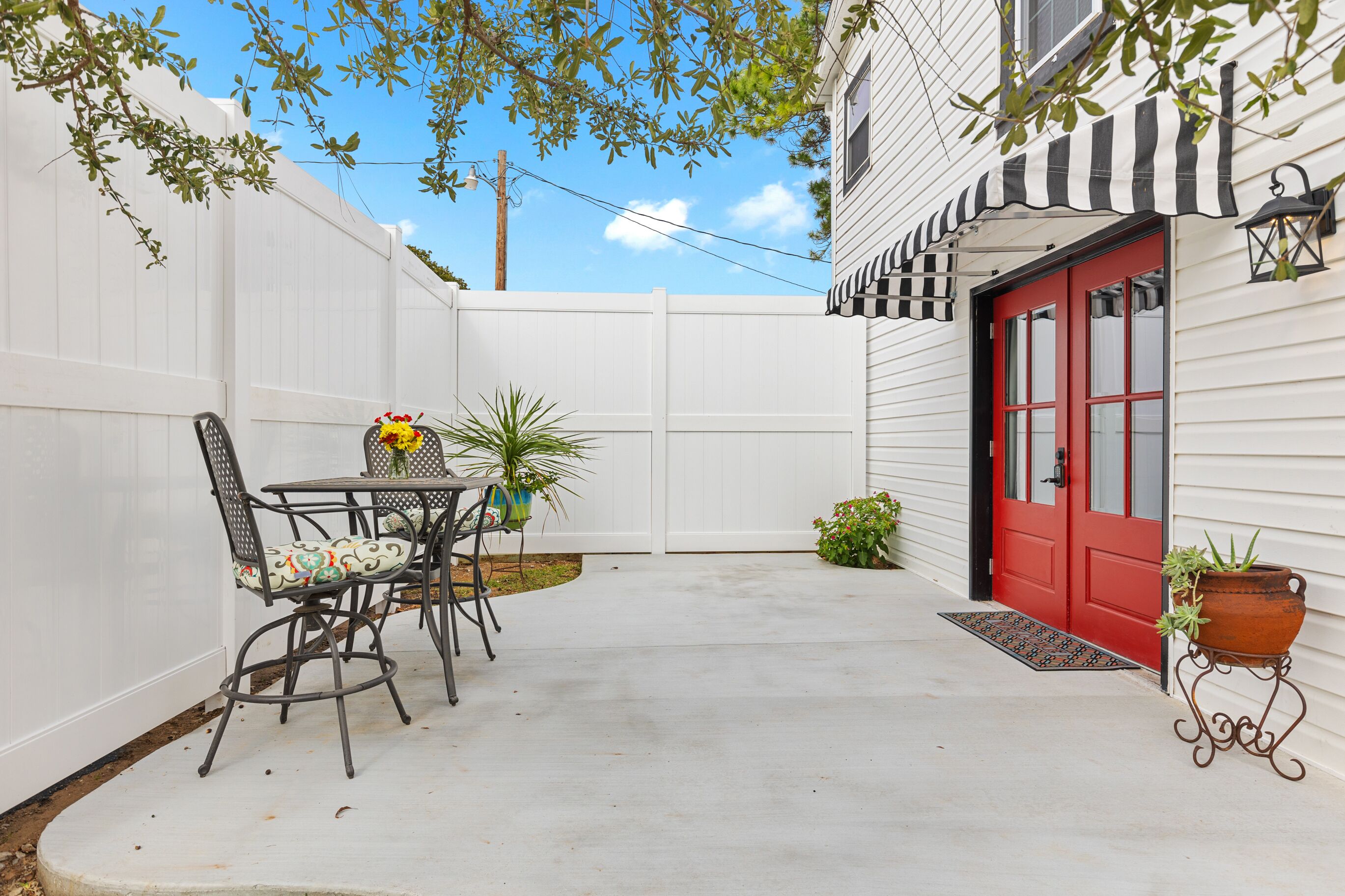 A patio with a table and chairs, a red door, and a white fence.