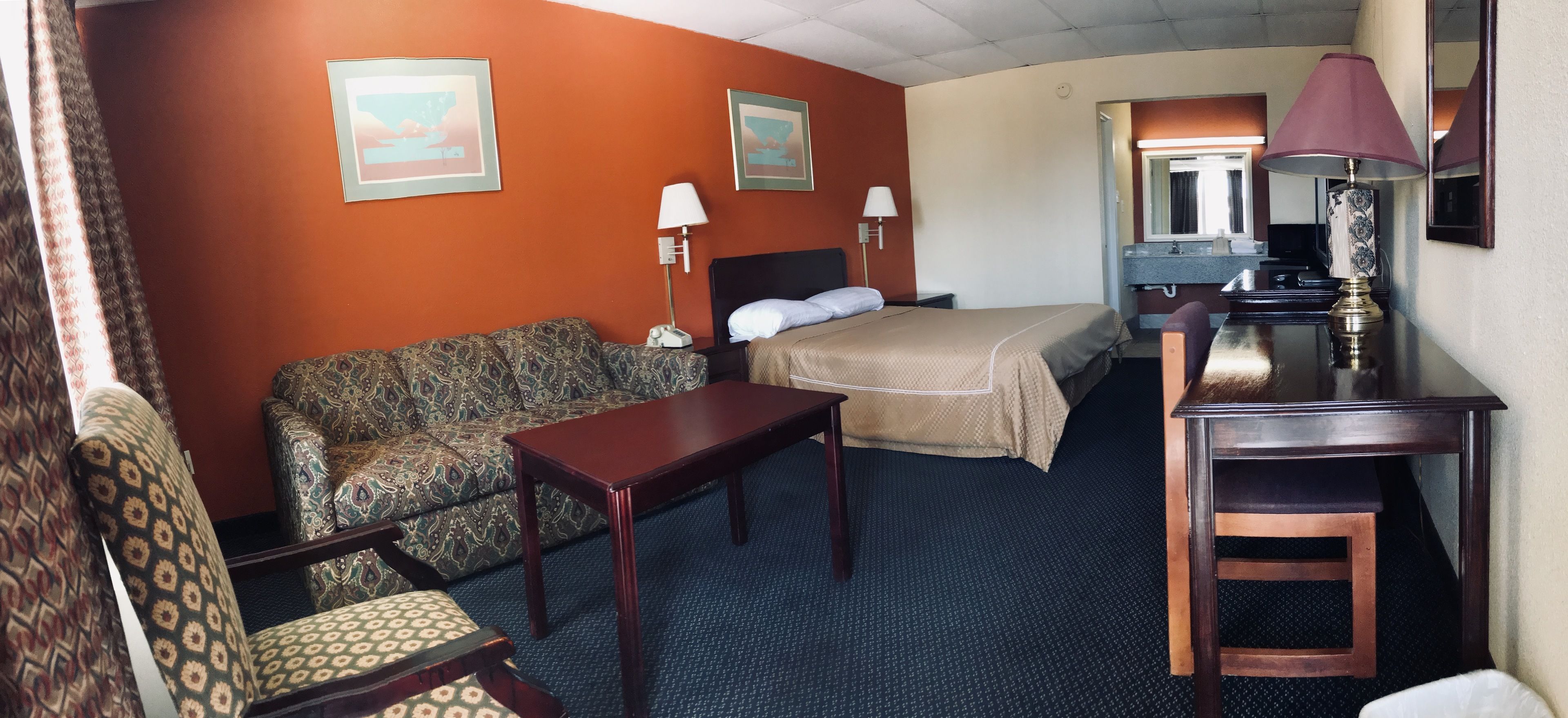 A hotel room with a bed, a patterned sofa, a small table, a lamp, and a mirror.