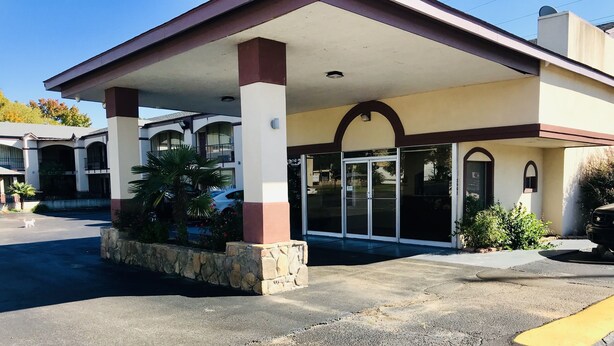 A building with a covered entrance, stone planter with plants, and a parking area. - Executive Inn (Texarkana)