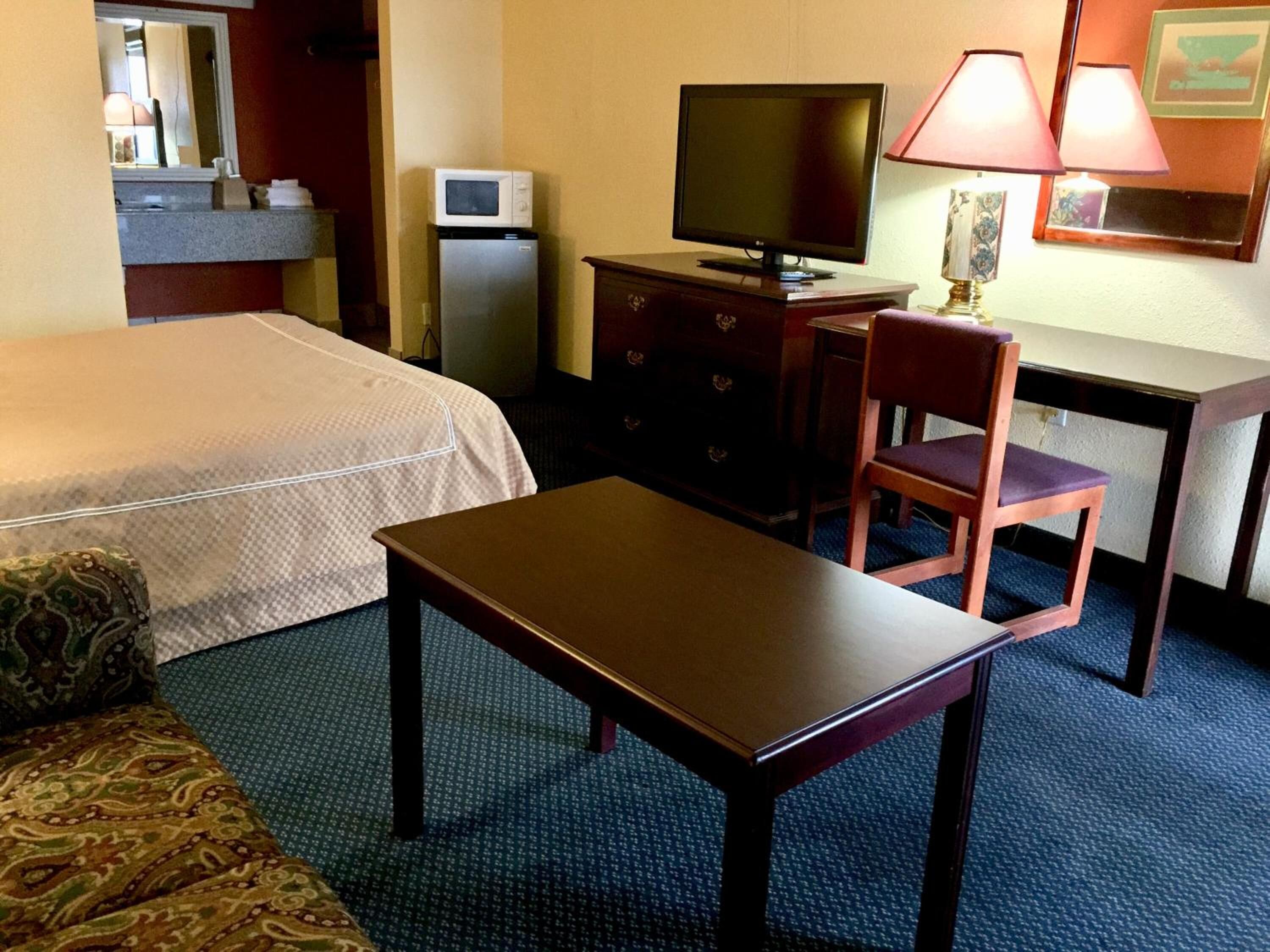 A hotel room with a bed, a desk, a chair, a television, a microwave, and a lamp.