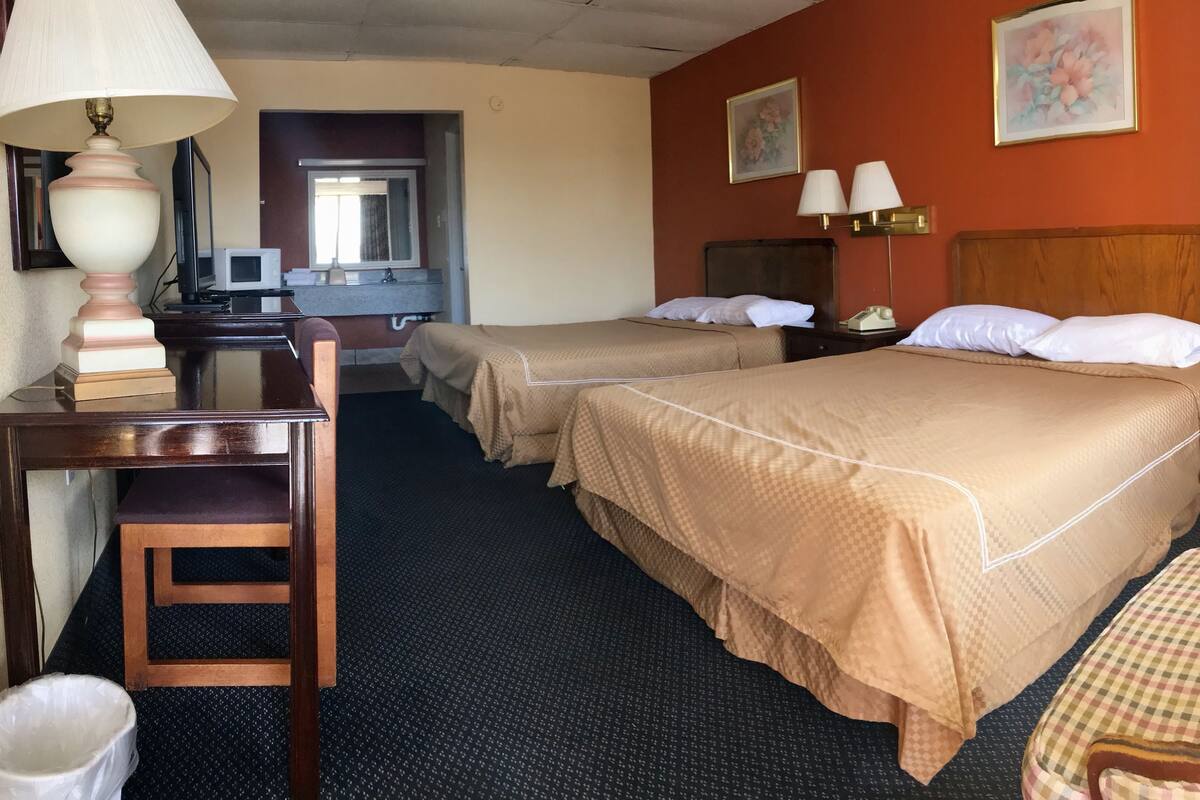 A hotel room with two beds, a desk, a chair, and a trash bin.