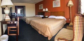 A hotel room with two beds, a desk, a chair, and a trash bin.