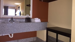 A bathroom with a granite countertop, a sink, a mirror, a towel rack, and a wooden bench. - Executive Inn (Texarkana)