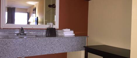 Un baño con encimera de granito, lavamanos, espejo, toallero y banco de madera.