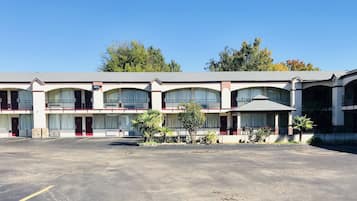 Un motel con varias habitaciones, un estacionamiento y algo de jardinería.