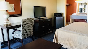 A hotel room with a bed, a desk with a lamp, a television, a refrigerator, and a chair. - Executive Inn (Texarkana)