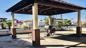 A covered outdoor area with a barbecue grill, a folding chair, and a concrete floor. - Executive Inn (Texarkana)