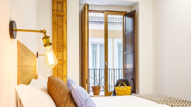 A hotel room with a bed, a wooden headboard, a wall-mounted lamp, and a view of the outside balcony.