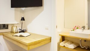 A modern bathroom with a wooden vanity, a mounted television, a sink with a mirror, and a towel rack.