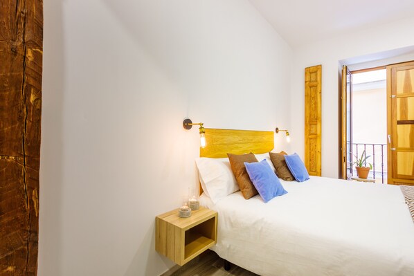 A neatly made bed with white linens and multiple pillows, a bedside table with a lamp, and a wooden headboard. - Jardines Boutique (Madrid)
