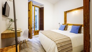 A bedroom with a bed, a desk, a chair, and a TV.