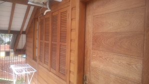 A wooden door with a metal handle, a window with wooden shutters, and an air conditioning unit mounted on the wall. - Apartamento Theobald (Tres Coroas)