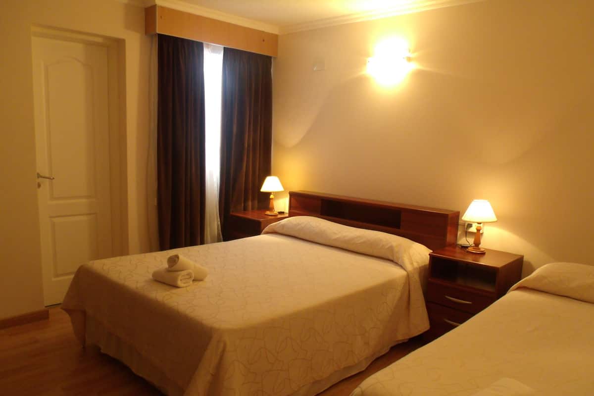 A hotel room with two beds, a wooden headboard, bedside tables with lamps, a door, and a curtain.