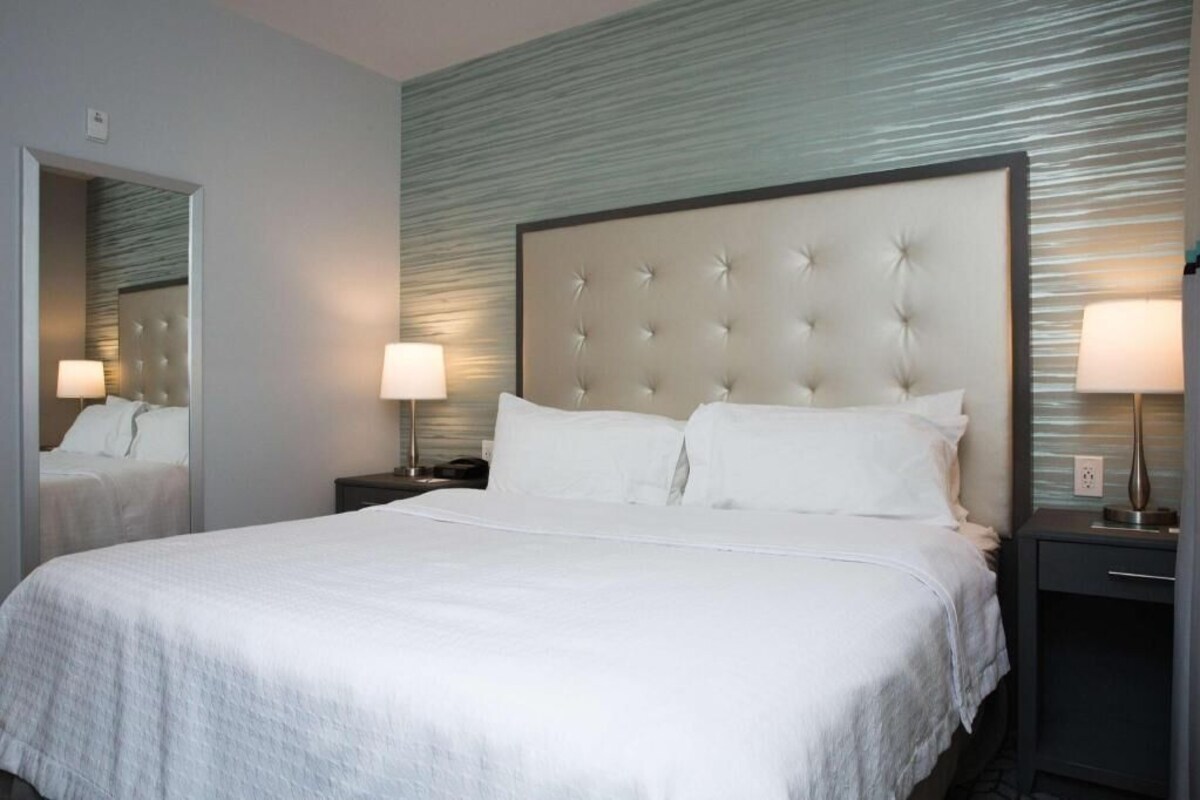 Habitación de hotel con una cama grande, dos mesitas de noche con lámparas, un espejo y una pared con textura.