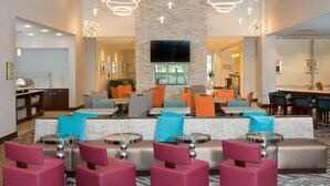 A modern hotel lobby with seating areas, a TV mounted on the wall, and a ceiling fan. - Homewood Suites by Hilton Allentown Bethlehem Center Valley (Center Valley)