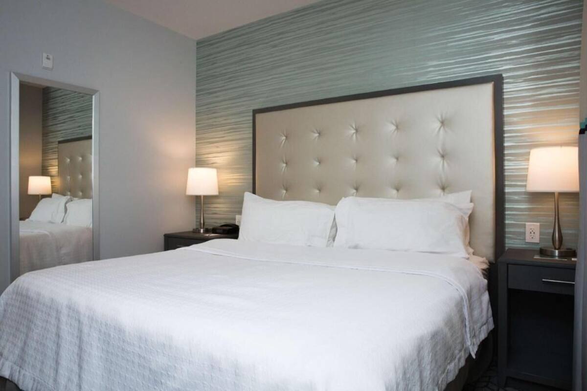 Habitación de hotel con una cama grande, dos mesitas de noche con lámparas, un espejo y una pared con textura.