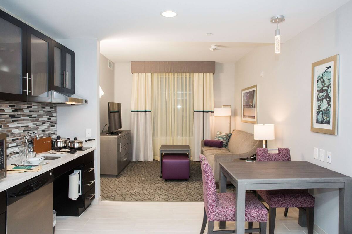 Una habitación de hotel compacta con kitchenette, comedor, sofá y una pequeña mesa.