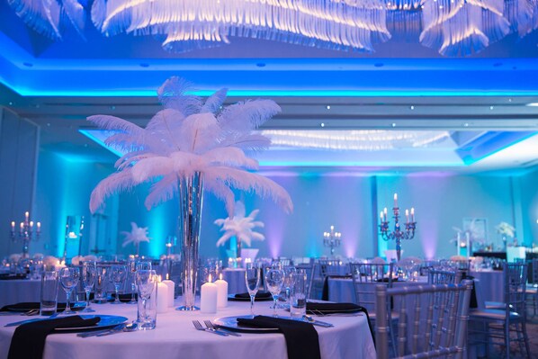 Un salón de banquetes con mesas dispuestas para un evento formal, con arreglos de plumas blancas y velas.