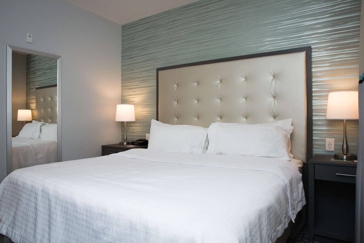 Habitación de hotel con una cama grande, dos mesitas de noche con lámparas, un espejo y una pared con textura.
