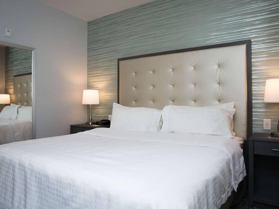 A hotel room with a large bed, two bedside tables with lamps, a mirror, and a textured wall.
