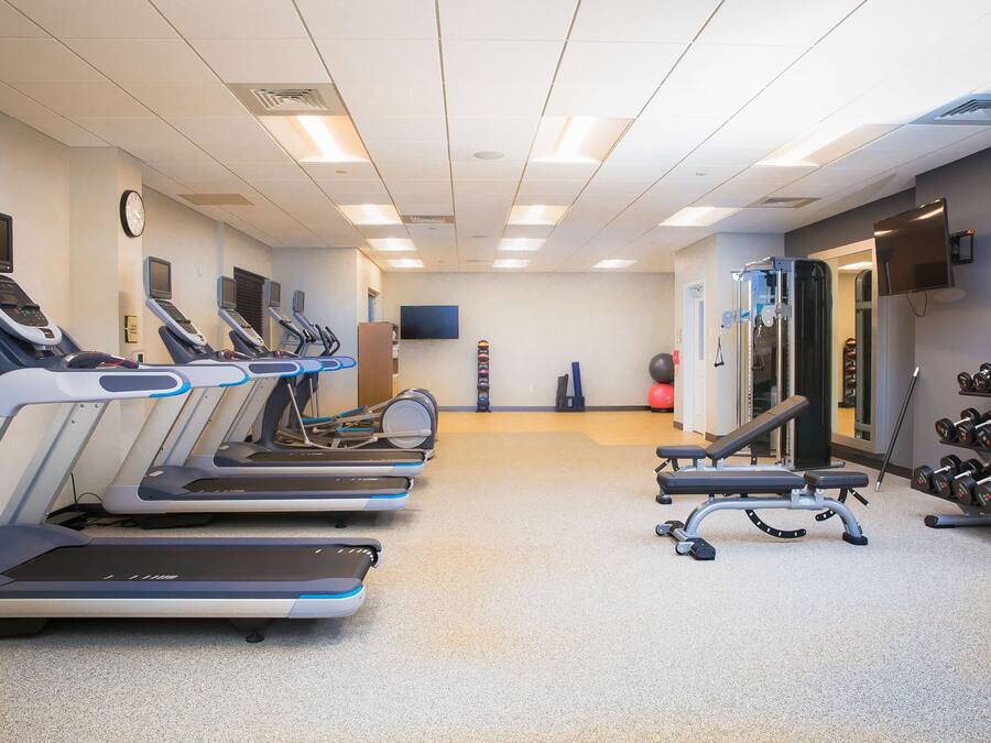 Un gimnasio con cintas de correr, una banca y mancuernas.