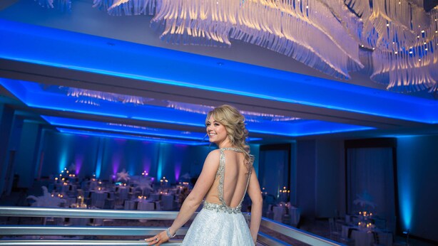 A woman in a dress with a backless design, standing in a room with a large, ornate chandelier and tables set for a formal event. - Homewood Suites by Hilton Allentown Bethlehem Center Valley (Center Valley)
