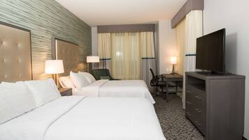 Quarto de hotel com duas camas, uma escrivaninha, uma televisão e uma cadeira.