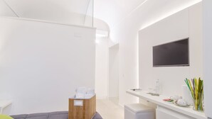 A modern, minimalist bathroom with a wooden bench, a white sink, and a flat-screen TV mounted on the wall. - Ortigia Bed and Breakfast (Syracuse)