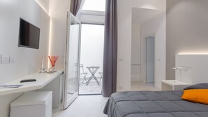 A modern hotel room with a bed, a desk, a TV, and a balcony with a table and chairs. - Ortigia Bed and Breakfast (Syracuse)