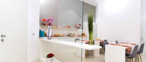 Una cocina moderna con encimera blanca, separador de vidrio y zona de comedor con mesa y sillas blancas.
