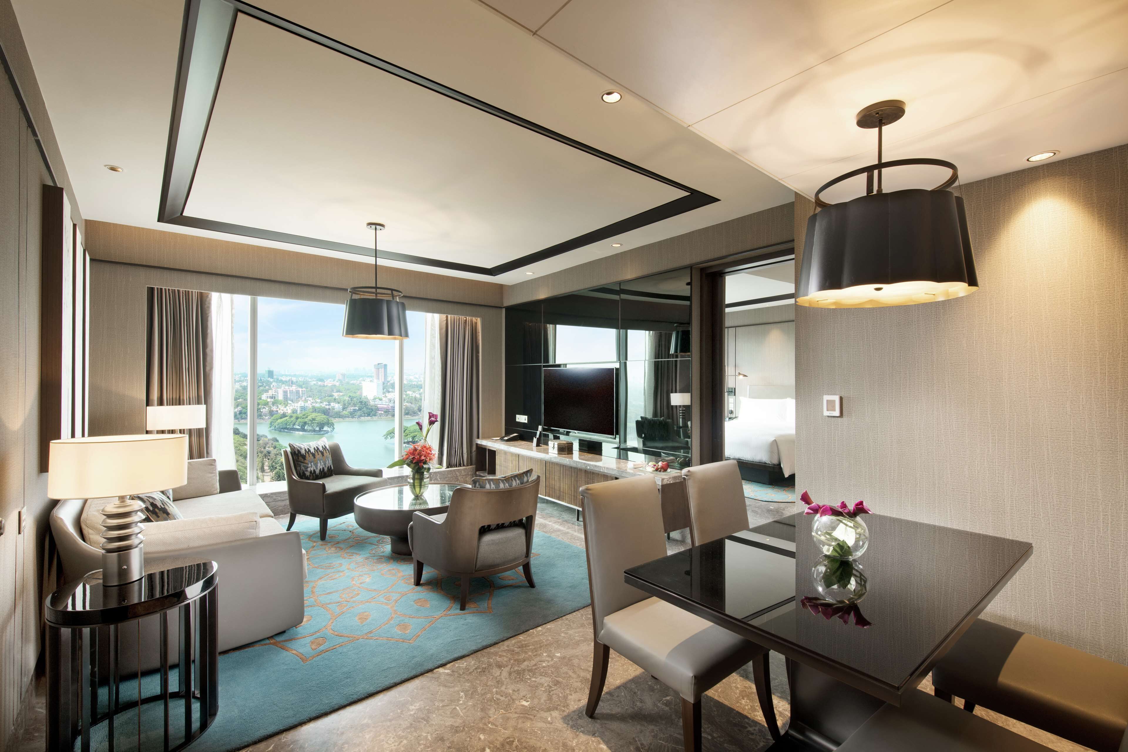 A modern hotel room with a dining area, a sofa, a TV, and a view of the city.