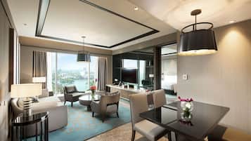 A modern hotel room with a dining area, a sofa, a TV, and a view of the city.