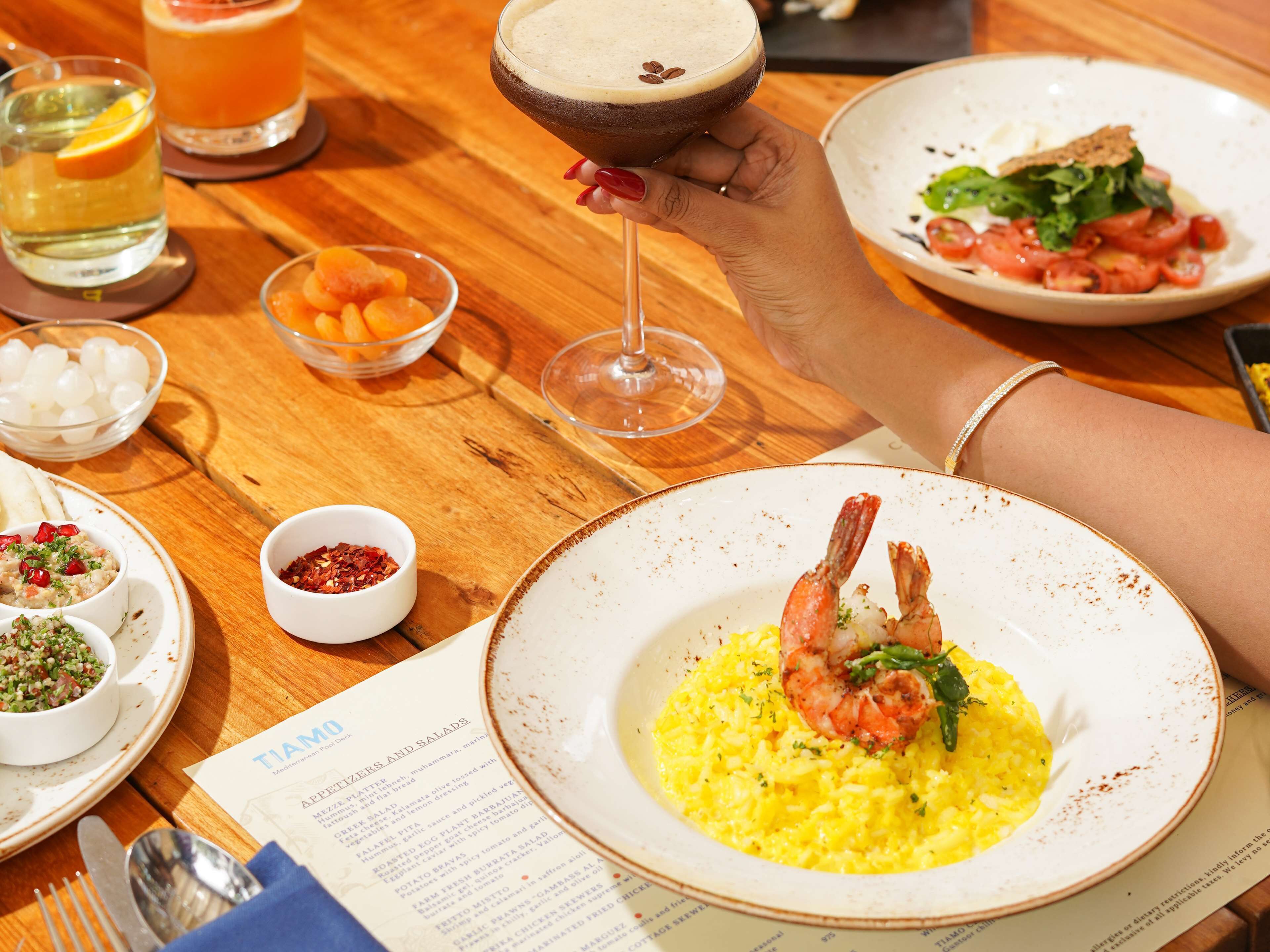 A dining table with various dishes, including shrimp on rice, a salad, and a cocktail.